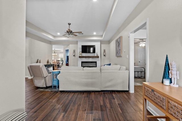 living room featuring a raised ceiling, ceiling fan, a fireplace, and dark hardwood / wood-style floors