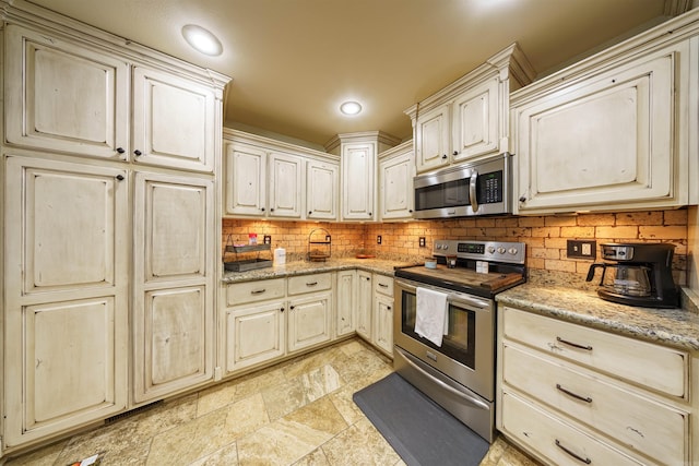 kitchen with decorative backsplash, light stone countertops, stainless steel appliances, and cream cabinetry