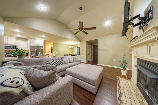 living room with ceiling fan with notable chandelier, dark wood-type flooring, vaulted ceiling, and a brick fireplace