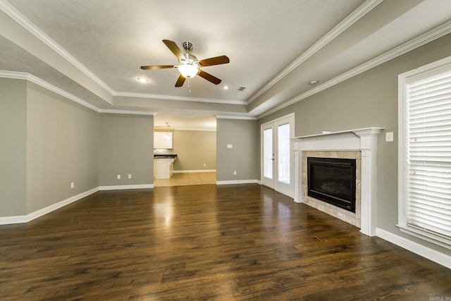 unfurnished living room featuring ceiling fan, a raised ceiling, dark hardwood / wood-style floors, crown molding, and a tiled fireplace