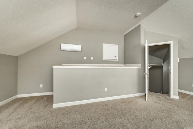 bonus room with vaulted ceiling, light carpet, a wall mounted air conditioner, and a textured ceiling