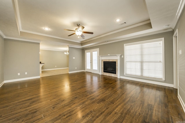 unfurnished living room with ceiling fan with notable chandelier, a raised ceiling, crown molding, dark hardwood / wood-style floors, and a fireplace