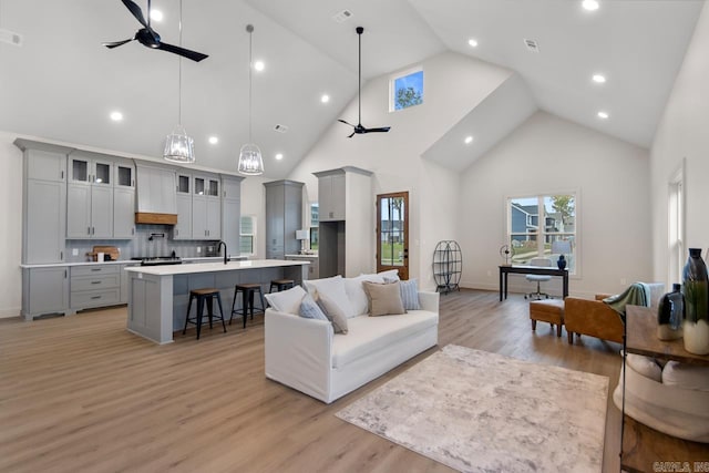 living room featuring ceiling fan with notable chandelier, light wood-type flooring, and high vaulted ceiling