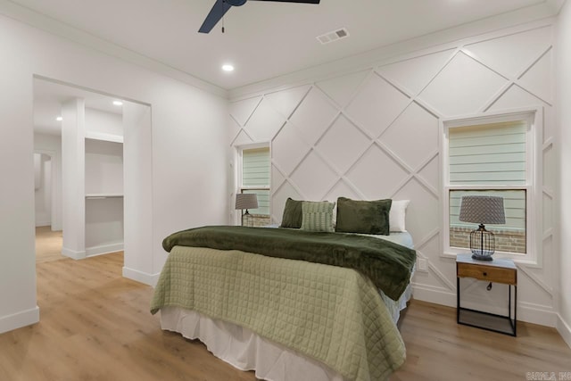 bedroom featuring light wood-type flooring, a spacious closet, ceiling fan, and crown molding