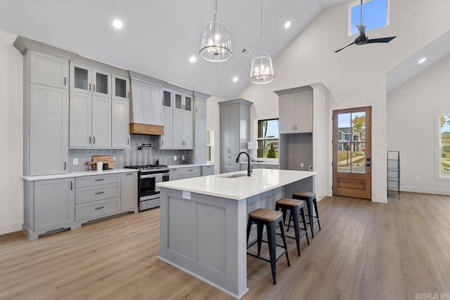 kitchen featuring gray cabinetry, gas range, ceiling fan with notable chandelier, a center island with sink, and high vaulted ceiling