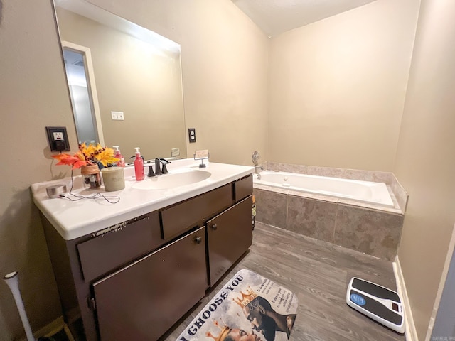 bathroom with hardwood / wood-style flooring, vanity, and tiled tub