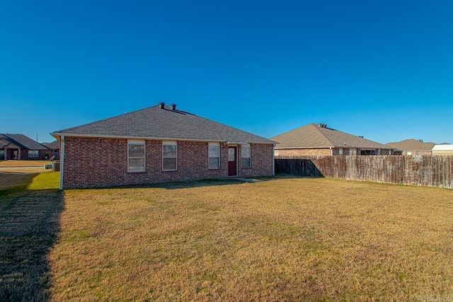 rear view of property with roof with shingles, brick siding, fence, and a lawn