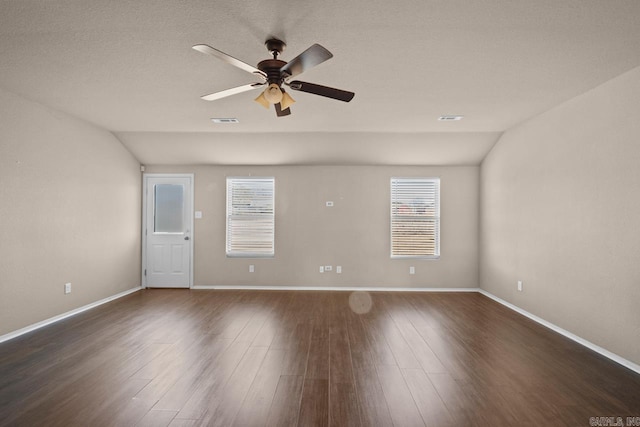 empty room featuring a ceiling fan, lofted ceiling, dark wood-style flooring, and visible vents