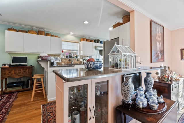 kitchen featuring white cabinets, light hardwood / wood-style floors, ornamental molding, and a breakfast bar area