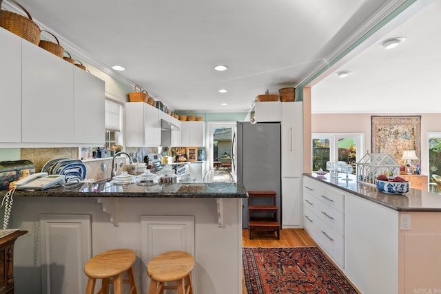 kitchen featuring kitchen peninsula, light hardwood / wood-style floors, a kitchen bar, white cabinets, and appliances with stainless steel finishes