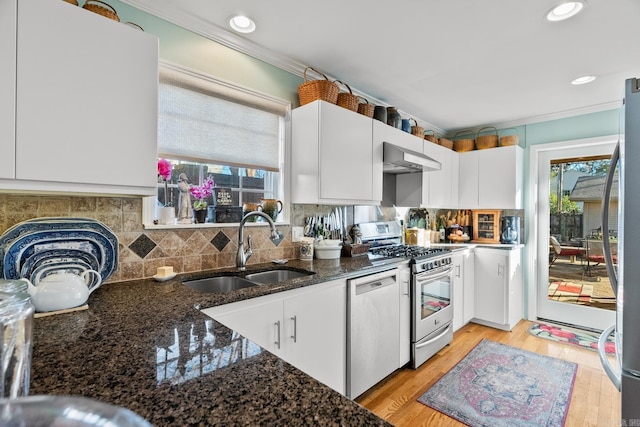 kitchen with sink, light hardwood / wood-style flooring, dark stone countertops, appliances with stainless steel finishes, and white cabinetry