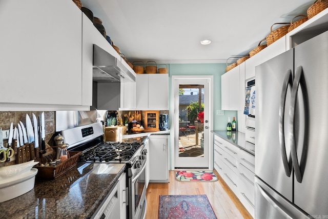 kitchen featuring dark stone counters, wall chimney exhaust hood, stainless steel appliances, light hardwood / wood-style flooring, and white cabinets