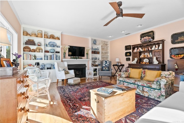 living room with hardwood / wood-style flooring, ceiling fan, crown molding, and built in shelves