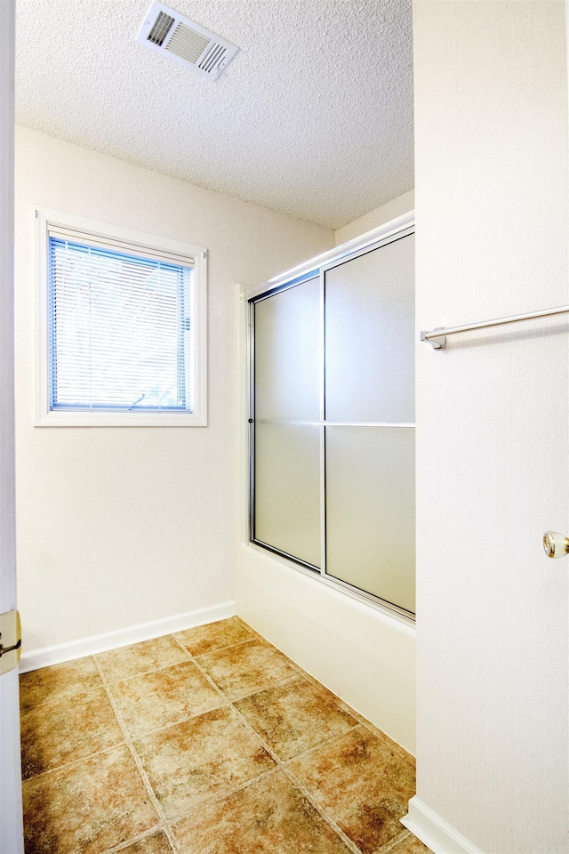 bathroom with a textured ceiling, tile patterned floors, and enclosed tub / shower combo