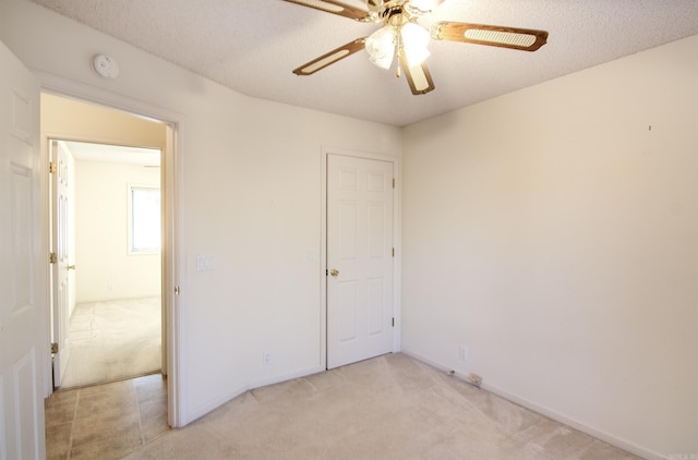 unfurnished bedroom with ceiling fan, light colored carpet, and a textured ceiling