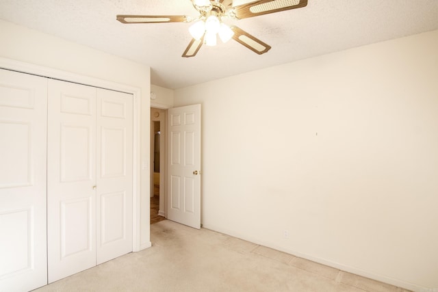 unfurnished bedroom with ceiling fan, a closet, light colored carpet, and a textured ceiling