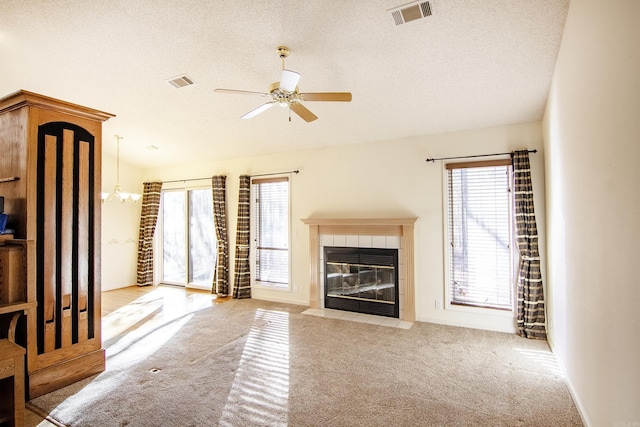 unfurnished living room featuring light carpet, a textured ceiling, ceiling fan with notable chandelier, and a tiled fireplace