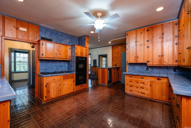 kitchen featuring tile countertops, ceiling fan, backsplash, and black double oven