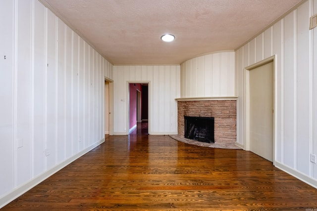 unfurnished living room with a stone fireplace, dark hardwood / wood-style flooring, and a textured ceiling