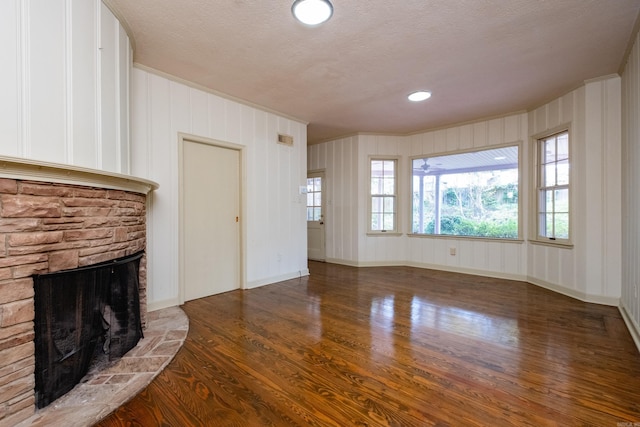 unfurnished living room featuring a textured ceiling, a stone fireplace, dark hardwood / wood-style floors, and ornamental molding