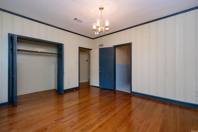 unfurnished bedroom with crown molding, a chandelier, a textured ceiling, a closet, and hardwood / wood-style flooring