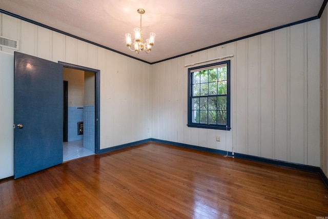 spare room with hardwood / wood-style floors, a textured ceiling, an inviting chandelier, and crown molding