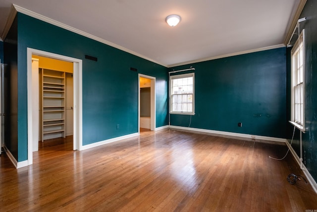 unfurnished bedroom with a closet, a spacious closet, crown molding, and wood-type flooring