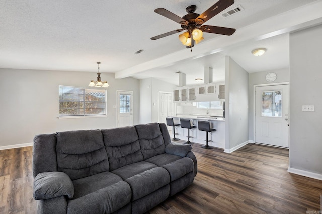 living room featuring a textured ceiling, dark hardwood / wood-style flooring, lofted ceiling with beams, and ceiling fan with notable chandelier