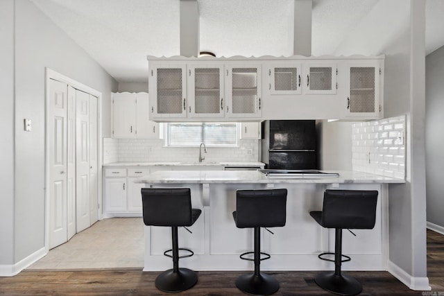 kitchen with hardwood / wood-style floors, a kitchen breakfast bar, black fridge, sink, and white cabinetry