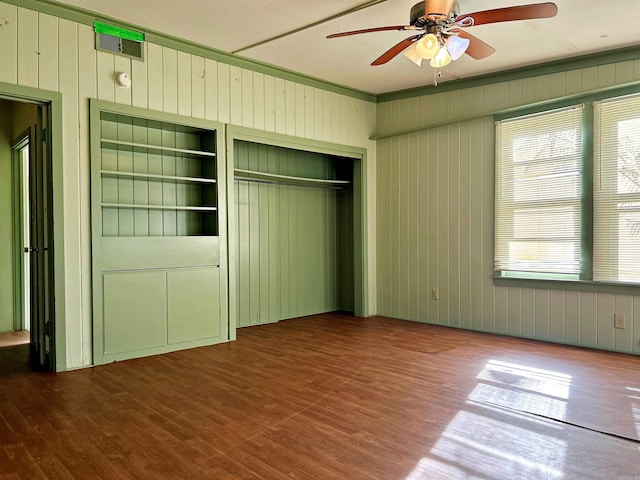 unfurnished bedroom with wood-type flooring, ceiling fan, and wooden walls