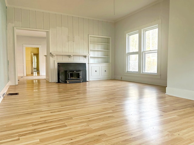 unfurnished living room featuring built in shelves, crown molding, and light wood-type flooring