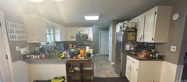 kitchen with kitchen peninsula, hardwood / wood-style floors, white cabinetry, and stainless steel refrigerator