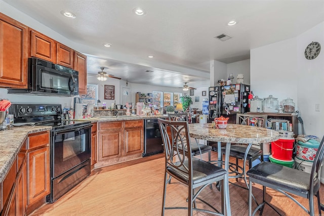 kitchen featuring black appliances, ceiling fan, light hardwood / wood-style floors, and light stone counters