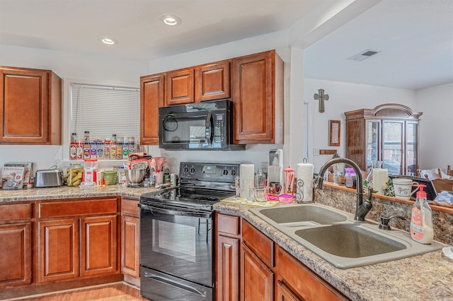 kitchen with black appliances, light stone counters, sink, and light hardwood / wood-style flooring