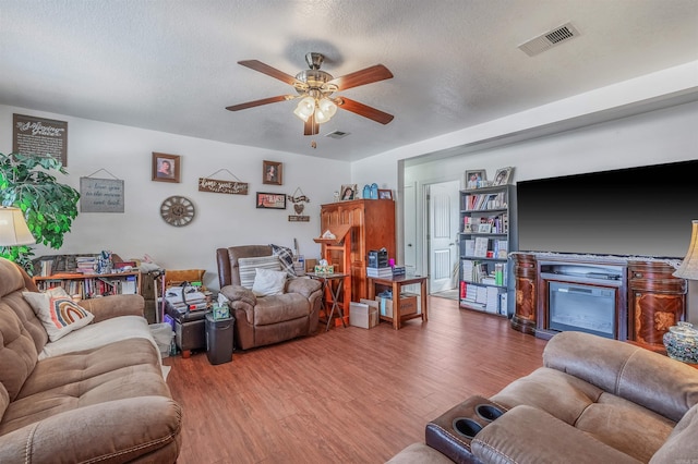 living room featuring wood-type flooring, a textured ceiling, and ceiling fan