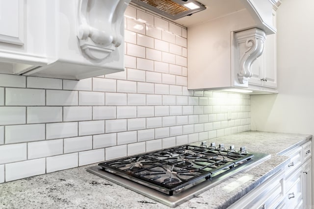 kitchen featuring stainless steel gas stovetop, light stone countertops, white cabinetry, and tasteful backsplash