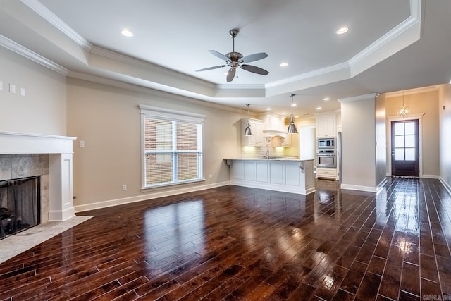 unfurnished living room featuring a raised ceiling, dark wood-type flooring, and ornamental molding