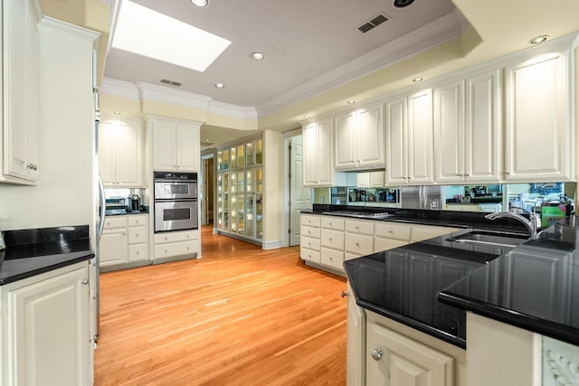 kitchen with a skylight, sink, stainless steel double oven, light hardwood / wood-style floors, and white cabinets