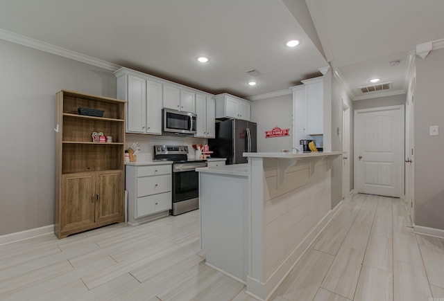 kitchen featuring white cabinets, a kitchen breakfast bar, ornamental molding, appliances with stainless steel finishes, and kitchen peninsula