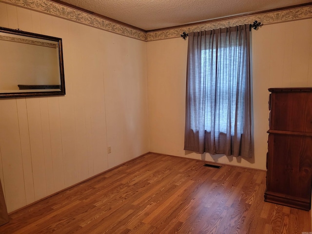 spare room with hardwood / wood-style flooring, a textured ceiling, and wooden walls