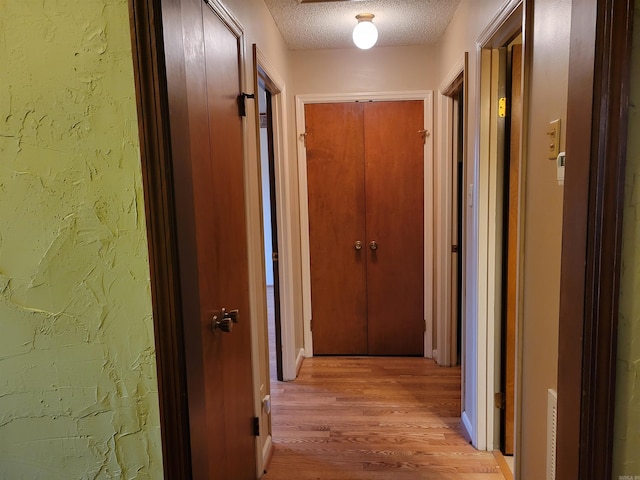 corridor featuring a textured ceiling and light hardwood / wood-style flooring