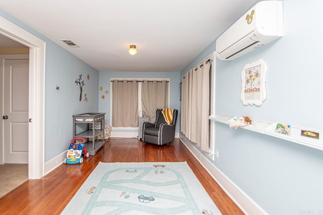 living area with a wall mounted air conditioner and hardwood / wood-style flooring