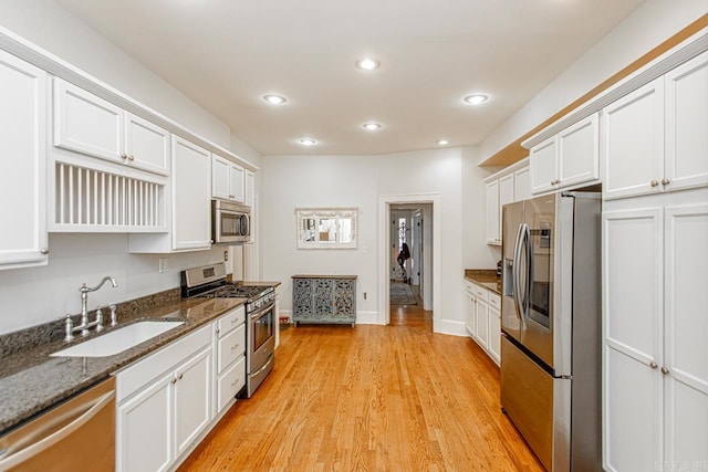 kitchen featuring appliances with stainless steel finishes, sink, light hardwood / wood-style flooring, dark stone countertops, and white cabinetry