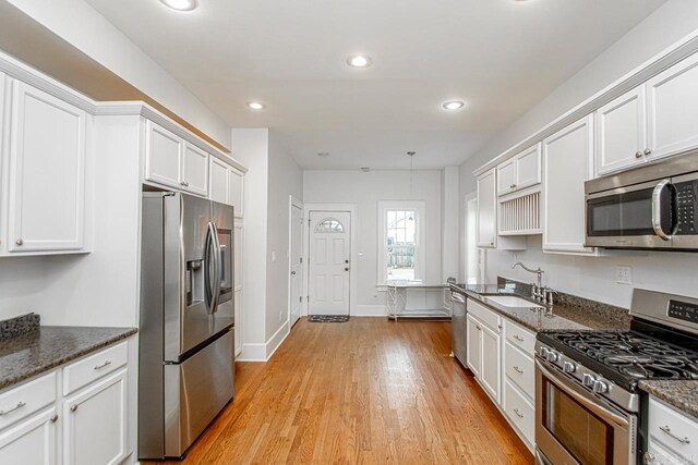 kitchen featuring white cabinetry, sink, stainless steel appliances, light hardwood / wood-style flooring, and dark stone countertops