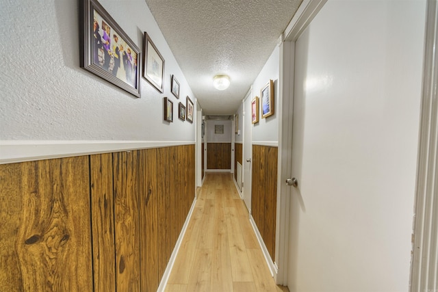 hall with wooden walls, light hardwood / wood-style floors, and a textured ceiling