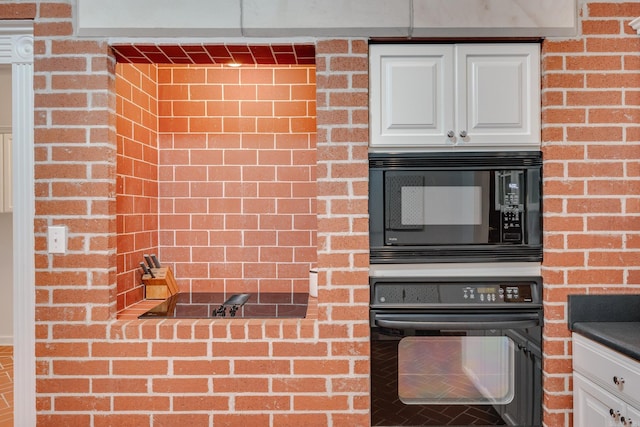 kitchen featuring white cabinets, black appliances, and brick wall