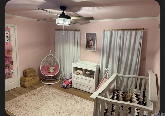 bedroom with a crib, light wood-type flooring, ceiling fan, and crown molding