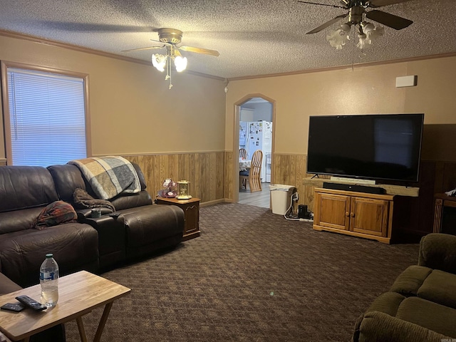 carpeted living room with ceiling fan, ornamental molding, a textured ceiling, and wooden walls