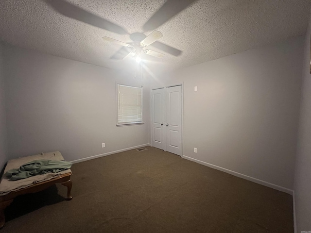 unfurnished bedroom featuring a textured ceiling, a closet, dark carpet, and ceiling fan