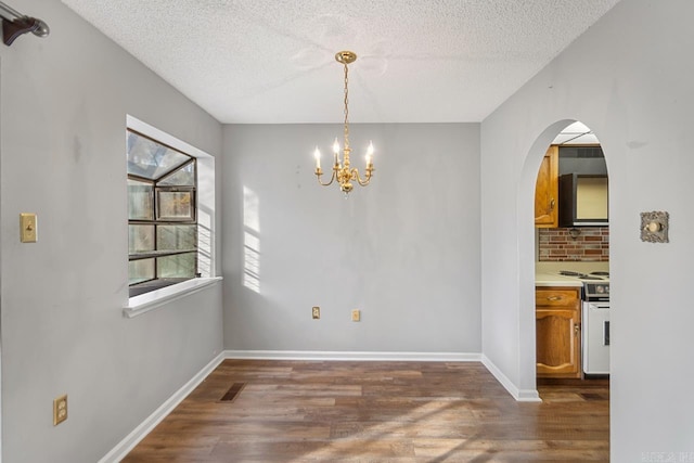 unfurnished dining area featuring a chandelier, a textured ceiling, and dark hardwood / wood-style floors